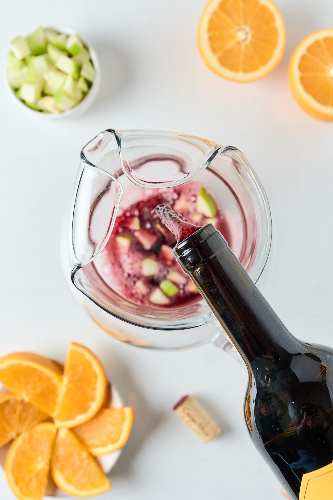 overhead view of sangria being made in a pitcher with orange slices and apples.