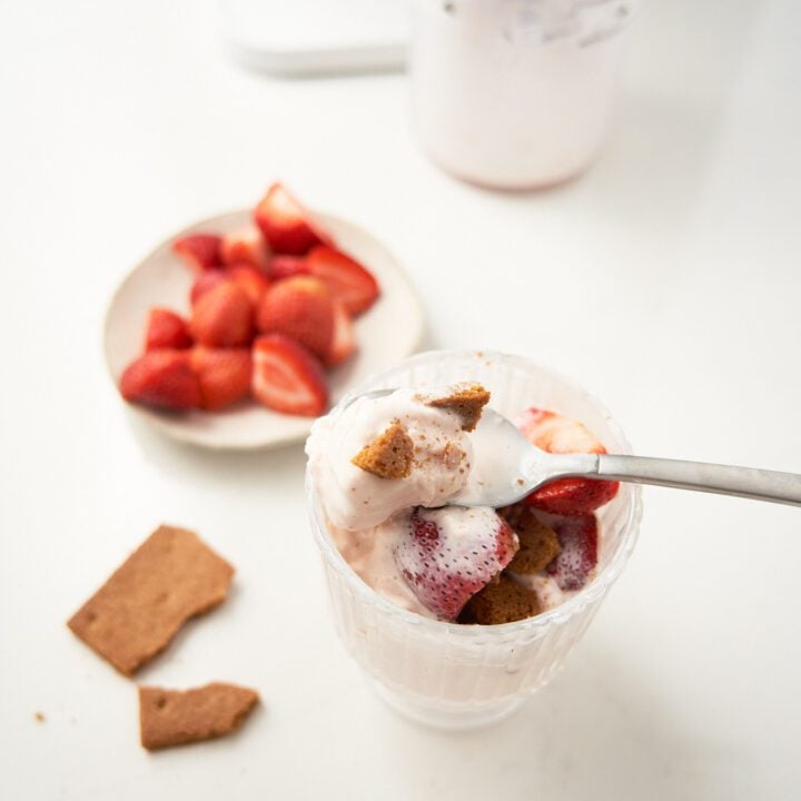 Ice cream on a glass container with strawberries on a plate and a cookie.