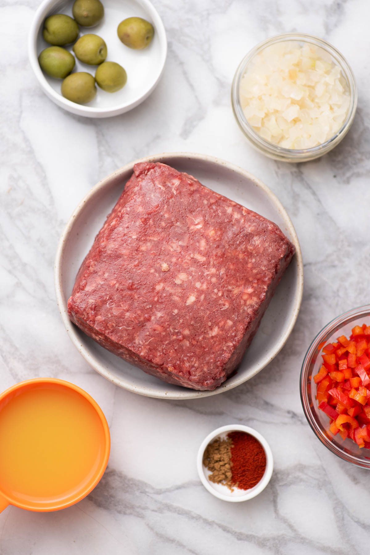 Ingredients for picadillo including ground beef, olives, onions and red peppers.