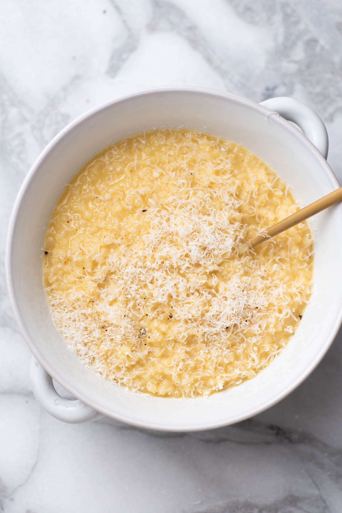 Pastina with shaved parmesan cheese and a spoon in a bowl.