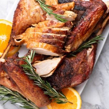 Carved turkey on a serving platter with orange slices and herbs.