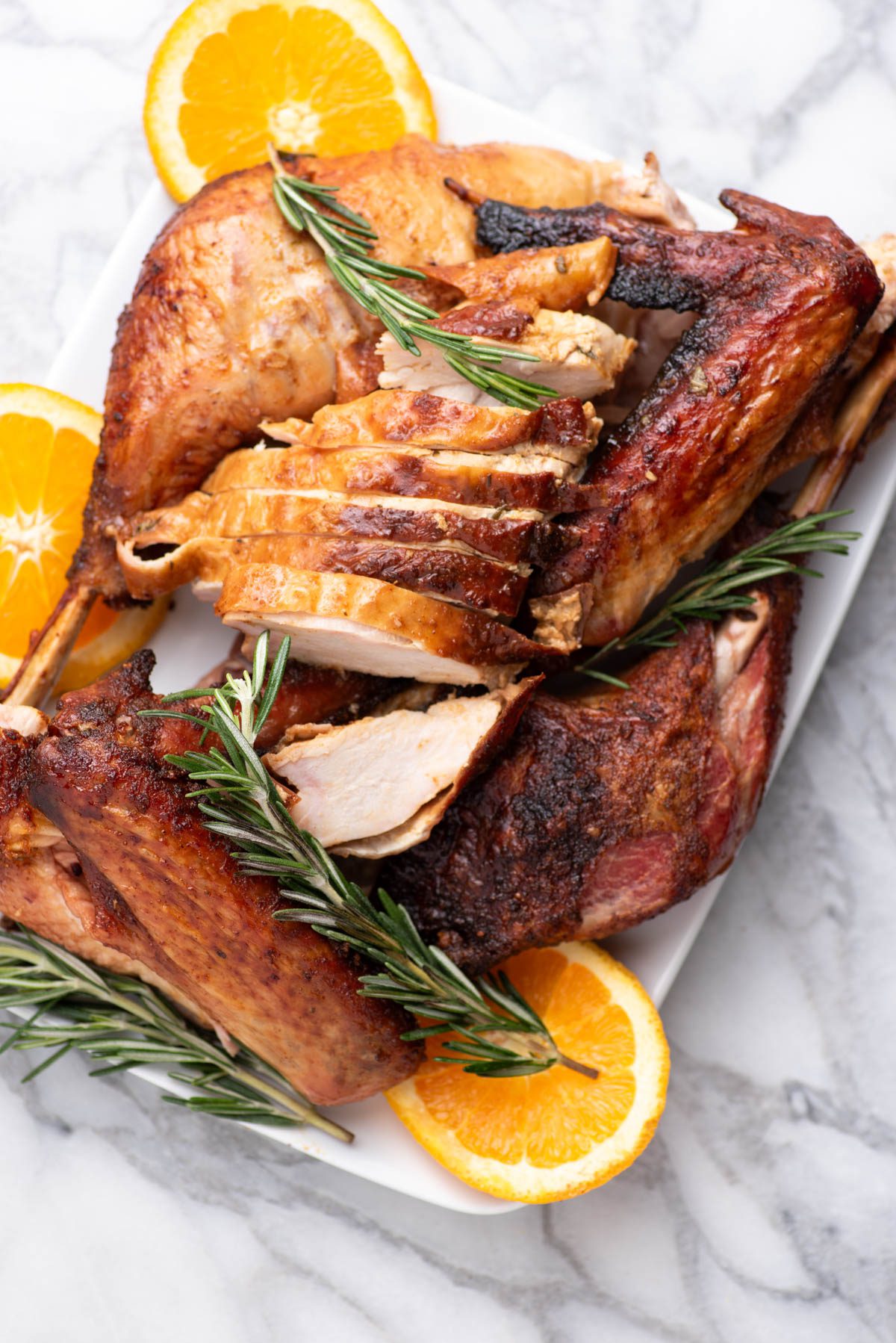 Carved turkey on a serving platter with orange slices and herbs.