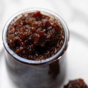 Bacon jam in glass jar with a butter knife on the side.