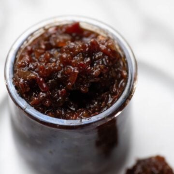 Bacon jam in glass jar with a butter knife on the side.