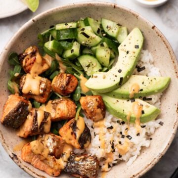 Salmon bites in a bowl with avocado, rice, cucumber and spicy mayo.