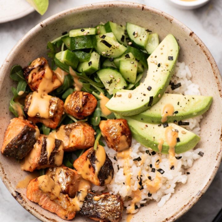 Salmon bites in a bowl with avocado, rice, cucumber and spicy mayo.