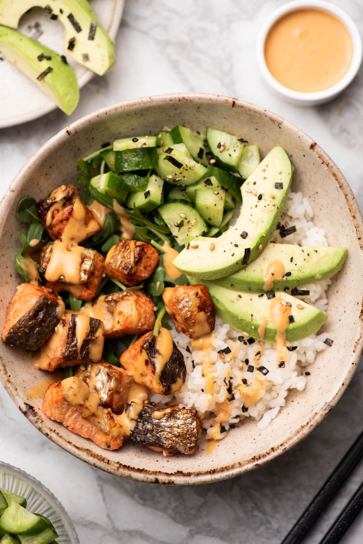 Salmon bites in a bowl with avocado, rice, cucumber and spicy mayo.