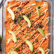 Sushi casserole topped with avocado slices, sriracha and mayo.