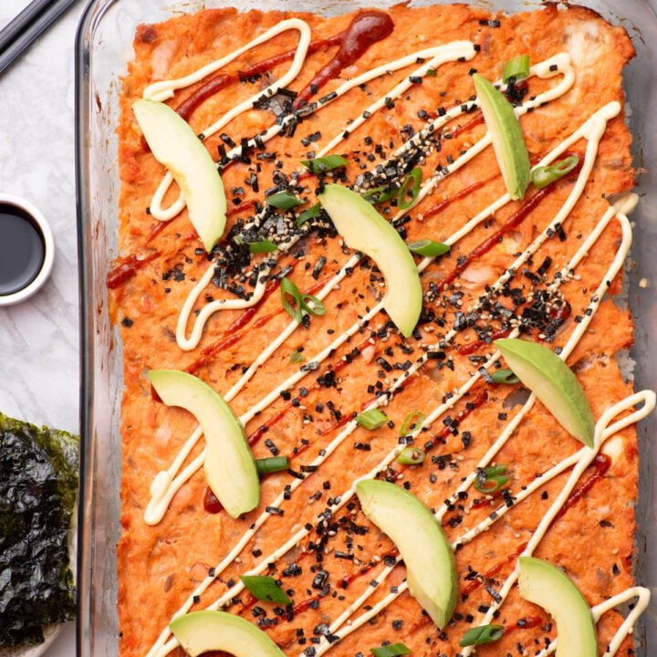 Sushi casserole topped with avocado slices, sriracha and mayo.