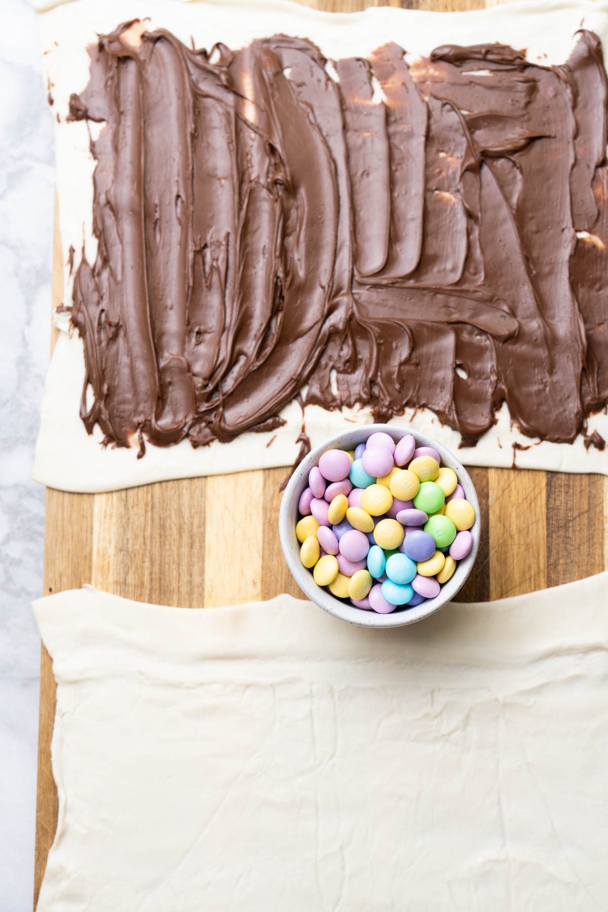 Puff pastry with Nutella on a wooden board. Bowl with Easter candy.
