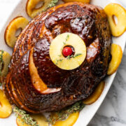 Easter ham with pineapple slices and cherry with thyme sprigs on a serving dish.