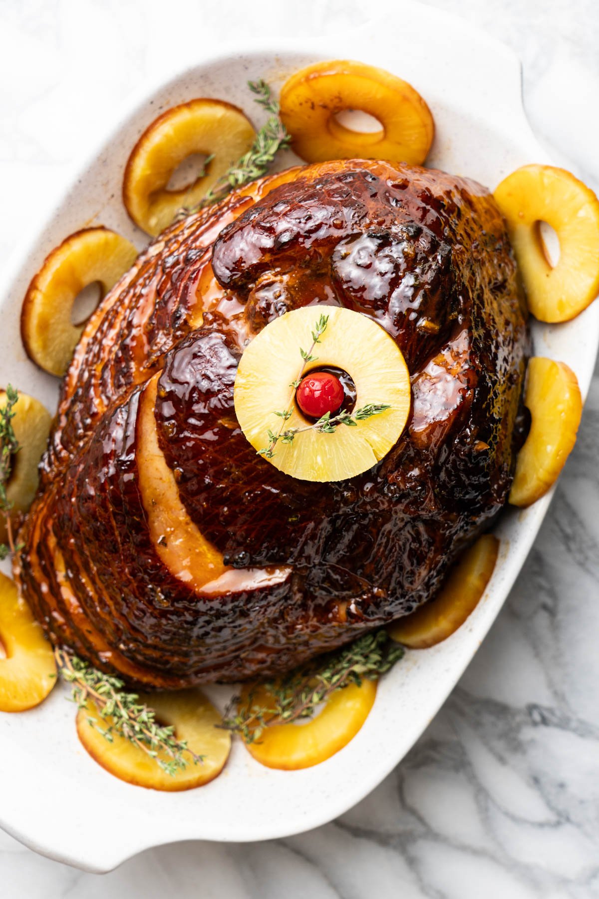 Easter ham with pineapple slices and cherry with thyme sprigs on a serving dish.