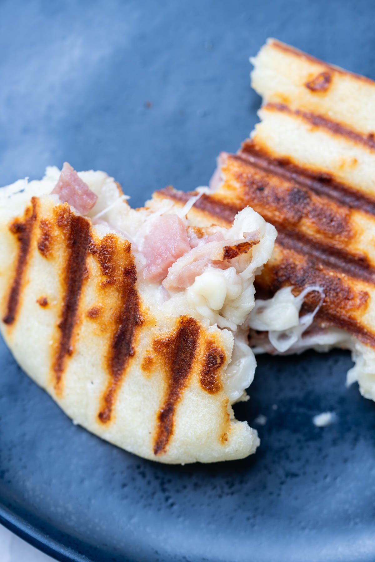 Colombian arepas stuffed with cheese and ham on a blue plate.