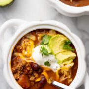Chili with sour cream, cilantro, avocado on a bowl with spoon.