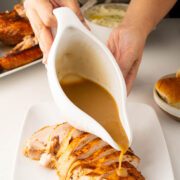 Gravy being poured over carved turkey from a gravy boat.