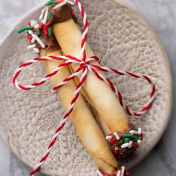 Barquillos dipped in chocolate and sprinkles and filled with dulce de leche. On a plate with a string bow.