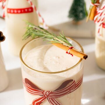 Coquito cocktail served in a glass garnished with a cinnamon stick and rosemary.