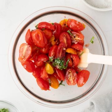 Marinated cherry tomatoes in a bowl with fresh herbs.