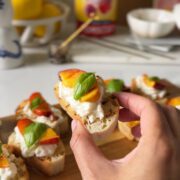 Peaches, burrata and bread with basil being held by hand with a wooden board in the background.