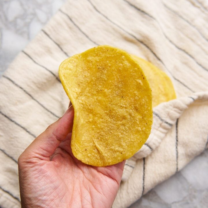 Corn tortillas wrapped in a kitchen towel. One tortilla being held by hand.