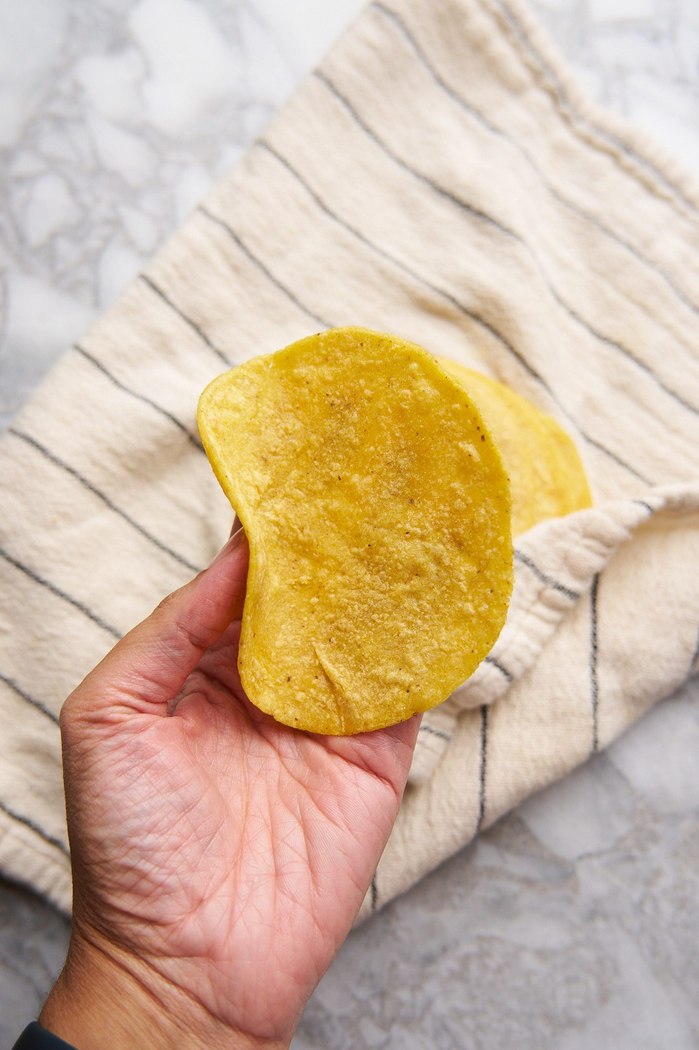 Corn tortillas wrapped in a kitchen towel. One tortilla being held by hand.