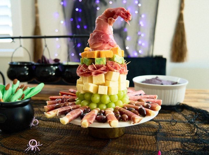 Charcuterie witch hat with grapes, cheese, salami and prosciutto placed on a cake stand.