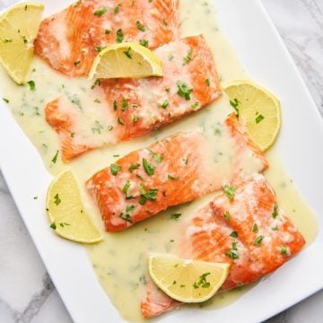 Salmon with lemon butter sauce on a plate garnished with lemon wedges and parsley.