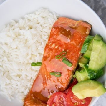 Maple balsamic glazed salmon in a bowl with rice and tomatoes, avocado and cucumber.