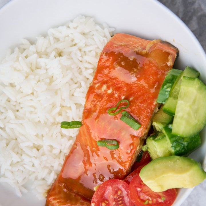 Maple balsamic glazed salmon in a bowl with rice and tomatoes, avocado and cucumber.