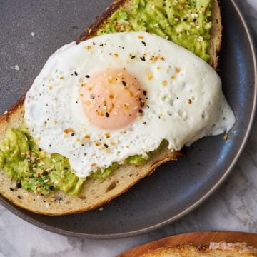 Sourdough avocado toast topped with an egg and everything but the bagel seasoning on a plate.