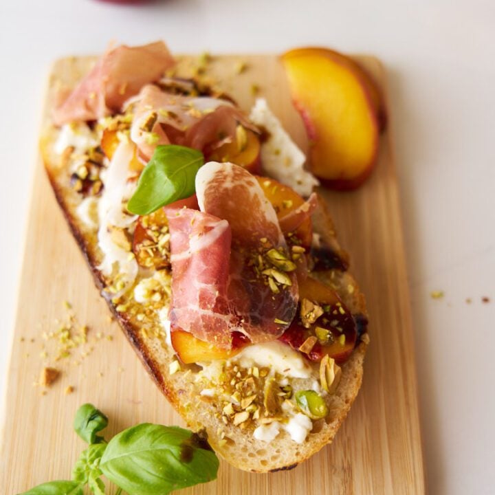 Burrata Toast with Peaches on a wooden board with basil.