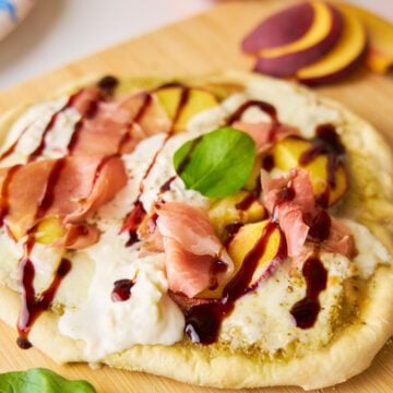 Burrata, peach, prosciutto flatbread on a cutting board.