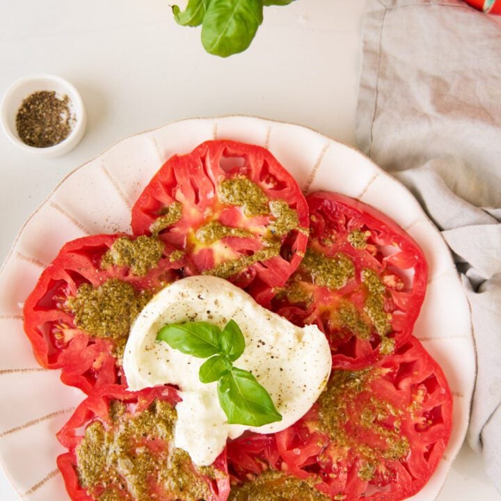 Burrata tomato salad on a platter dressed with pesto and garnished with basil.