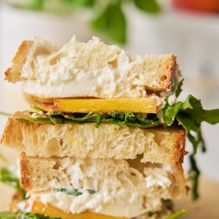 Sandwich with sourdough bread, arugula, burrata and peaches on parchment paper.