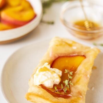 Peach and Burrata Upside Down Puff Pastries with honey and thyme on a plate.